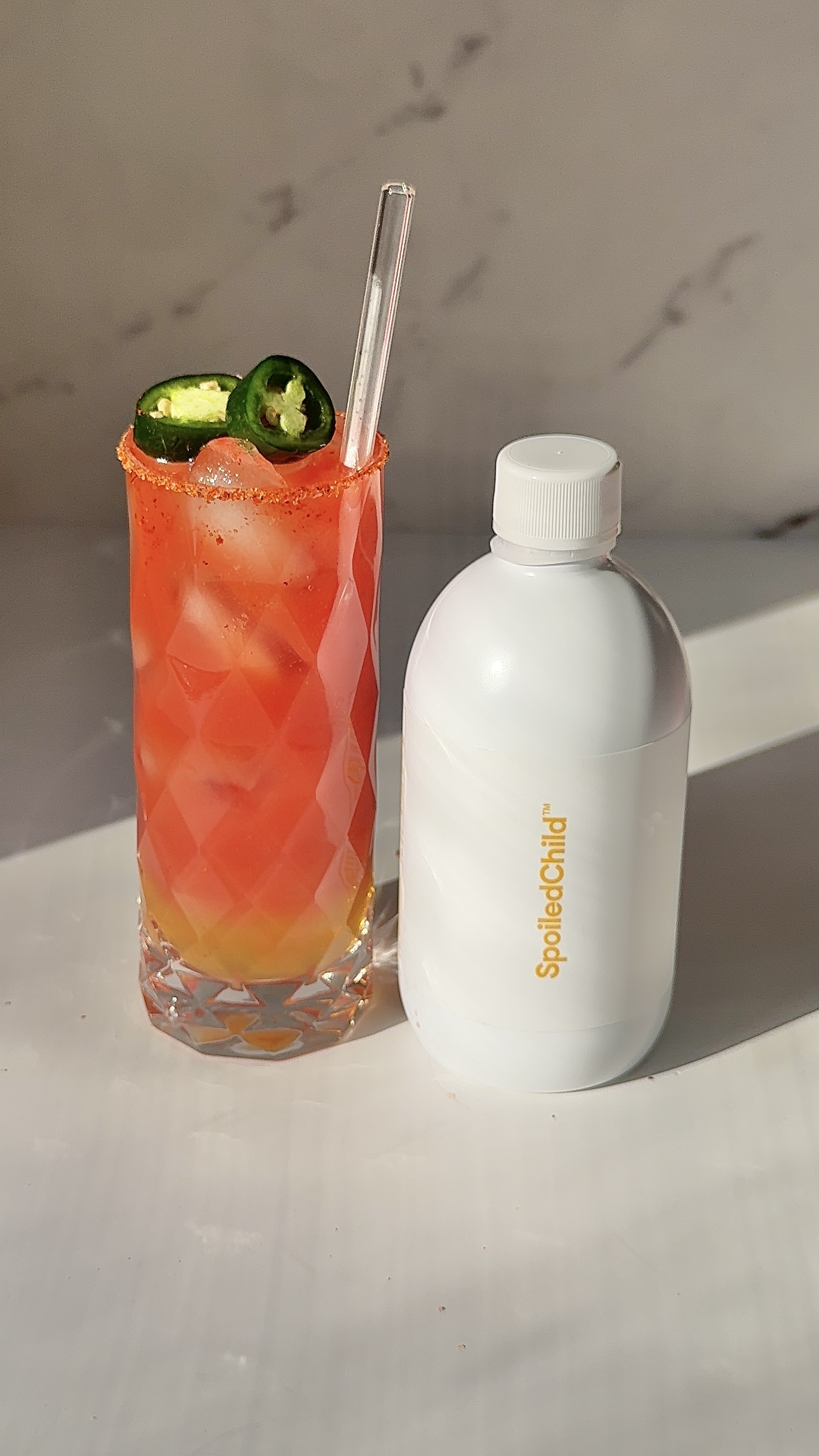 Tall glass of red guava collagen mocktail with a chili-salt rim and fresh jalapeño slices